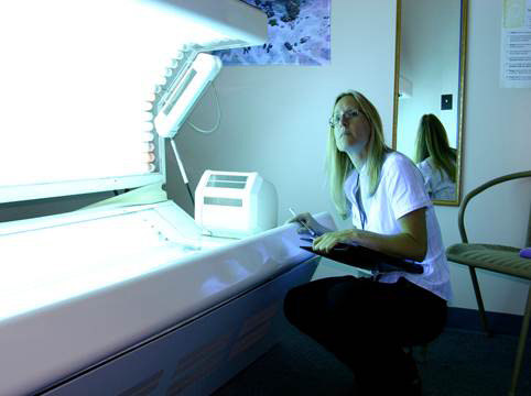 Woman squatting next to a tanning bed with a clipboard